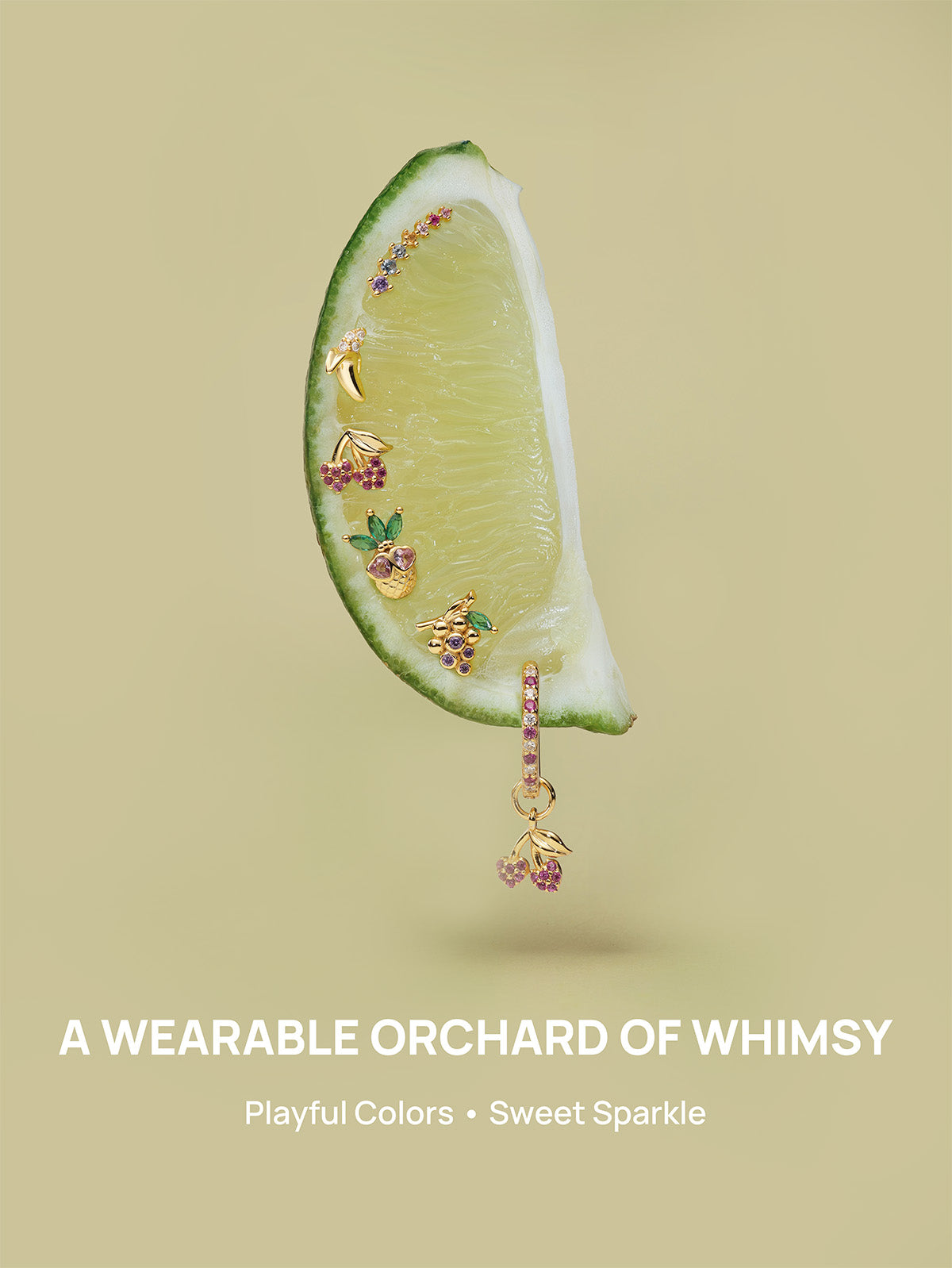 KOSINER Orchard whimsical fruit piercing jewelry arranged on fresh lime slice, includes banana, cherry, pineapple, grape flat studs and cherry dangle hoop, slogan A WEARABLE ORCHARD OF WHIMSY