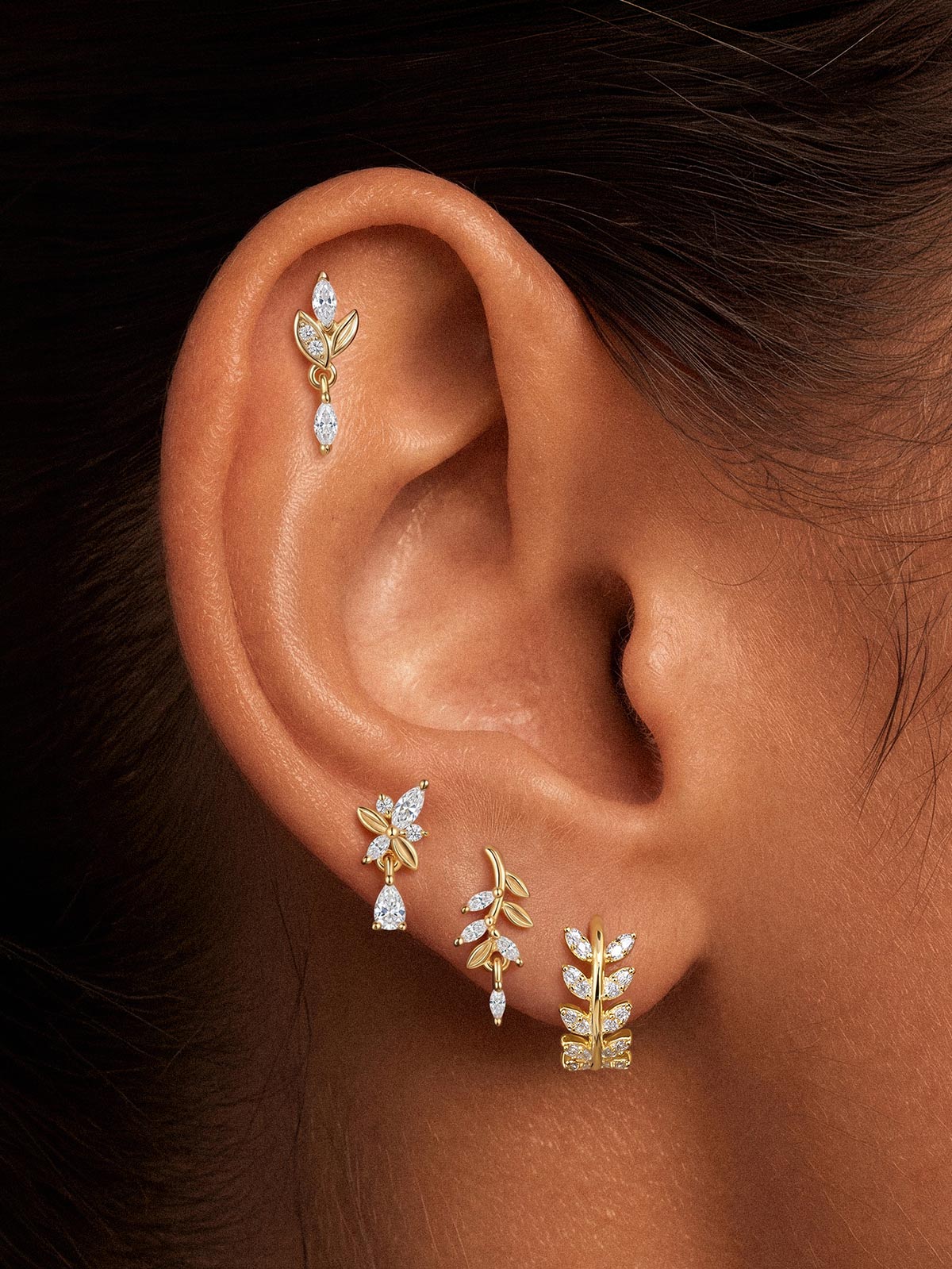 Close-up of KOSINER olive branch drop stud styled with gold botanical earrings