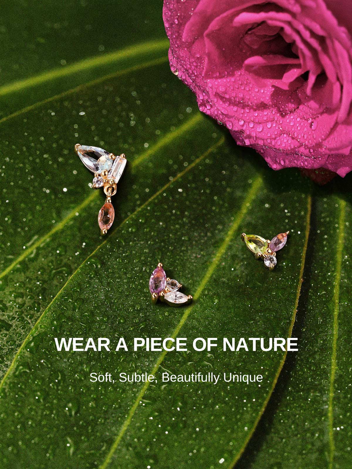 KOSINER Gem Garden nature-inspired multi-color gem piercing studs laid on dewy green leaves and magenta rose, featuring trio three-tone, pear dangle, butterfly multi-shape flat back designs