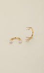 Pair of KOSINER 14K solid gold curved C barbell piercings, dual clear cubic zirconia gems secured by four-prong settings, laid flat on cream background