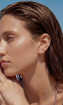 Beach lifestyle portrait of a model wearing KOSINER Seaspritz bikini series 14K gold flat back studs, sun-kissed wet hair and sandy hands, tropical seaside scenery for summer vacation jewelry inspiration