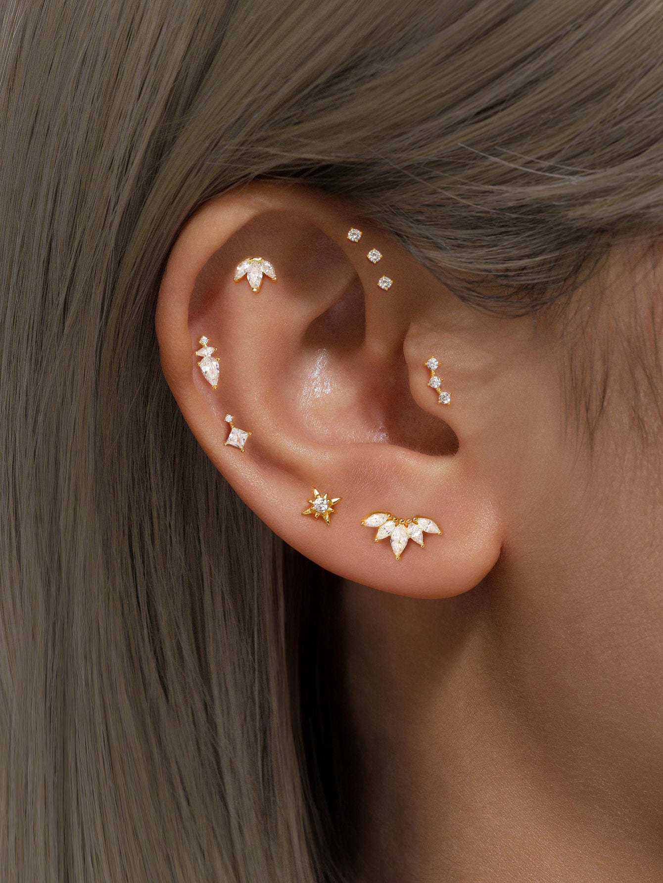 Gold sterling silver ear piercings with cubic zirconia, styled on ear. Square stud, starburst, lotus designs.
