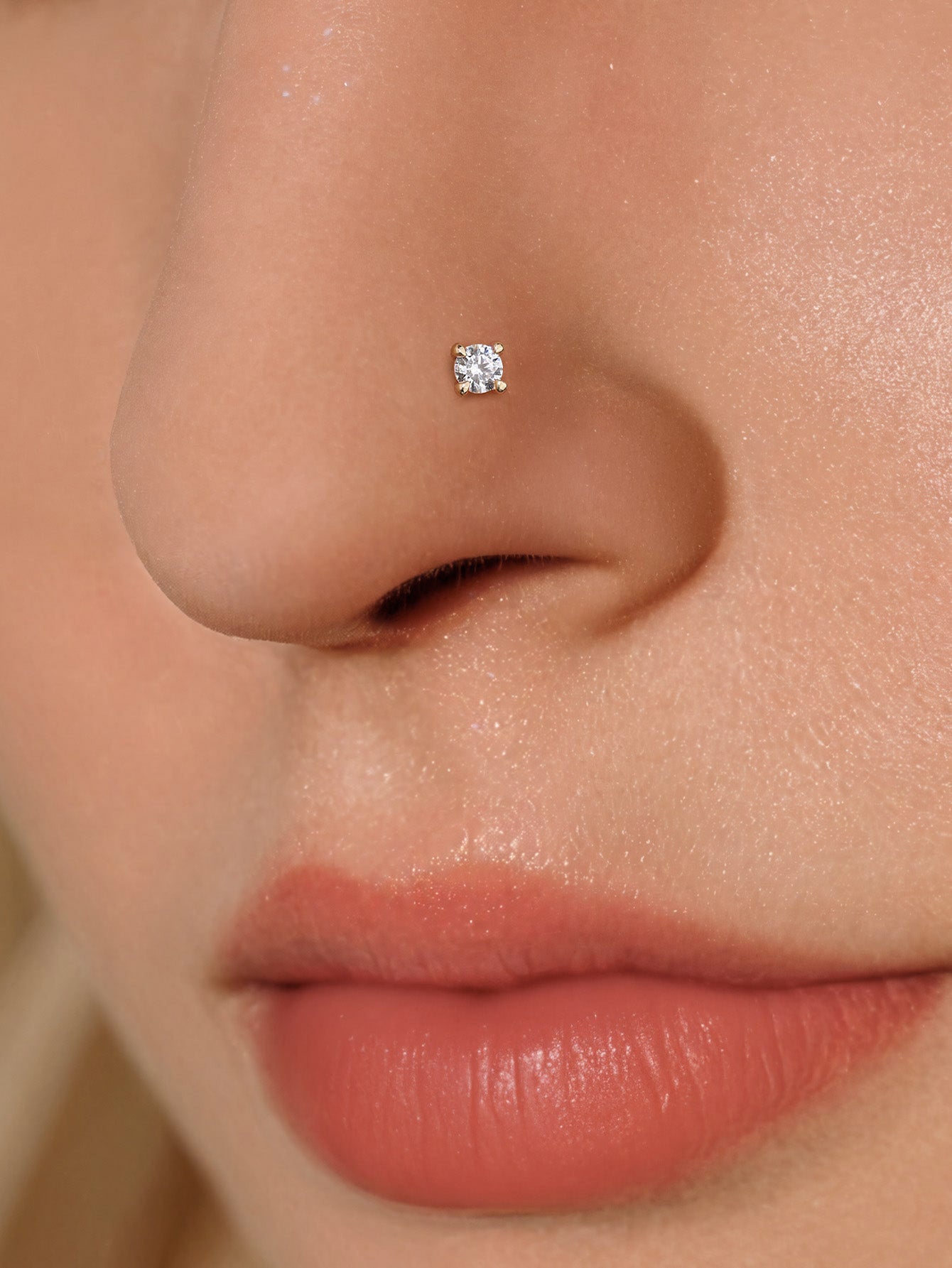 Macro close-up of KOSINER four-prong round stone twist nose stud securely fitted on nostril piercing, highlighting polished gold finish and sparkling center stone