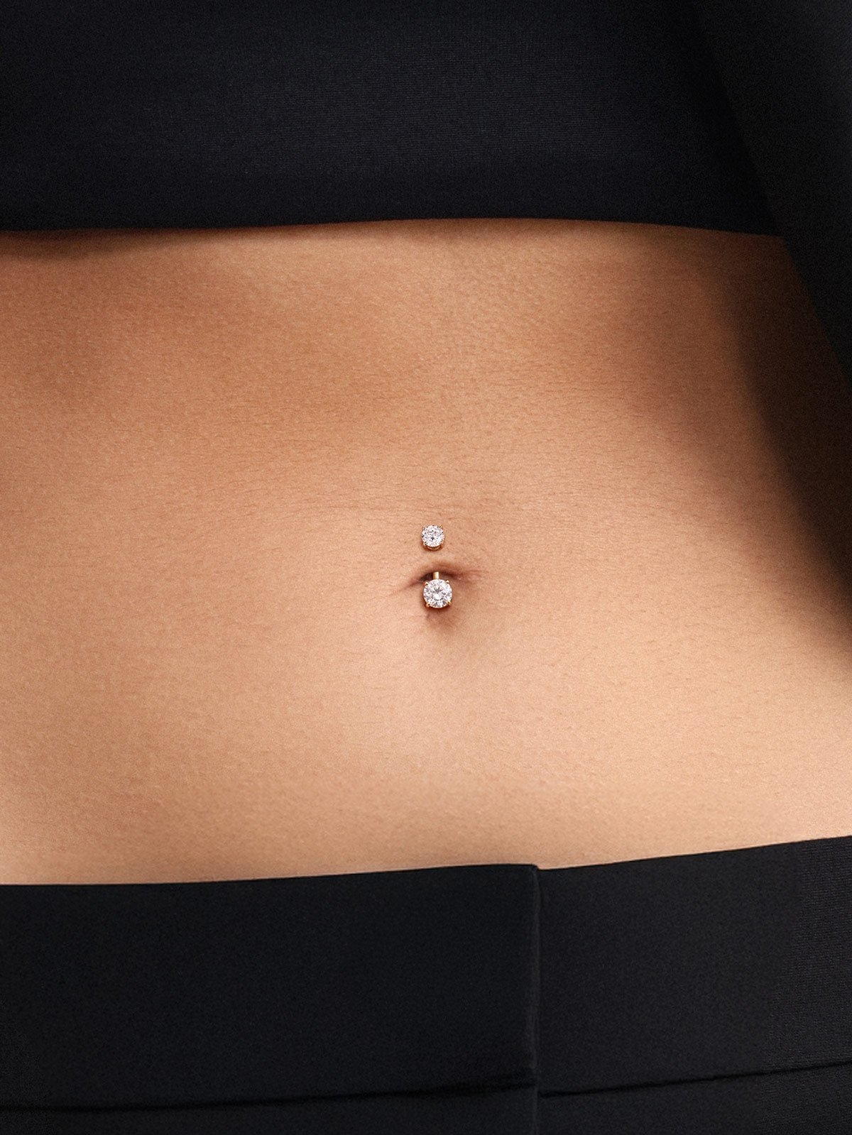 Full midsection lifestyle photo with model wearing black crop top and tailored trousers, subtle understated styling of tiny sized KOSINER 14K solid gold classic navel piercing stud