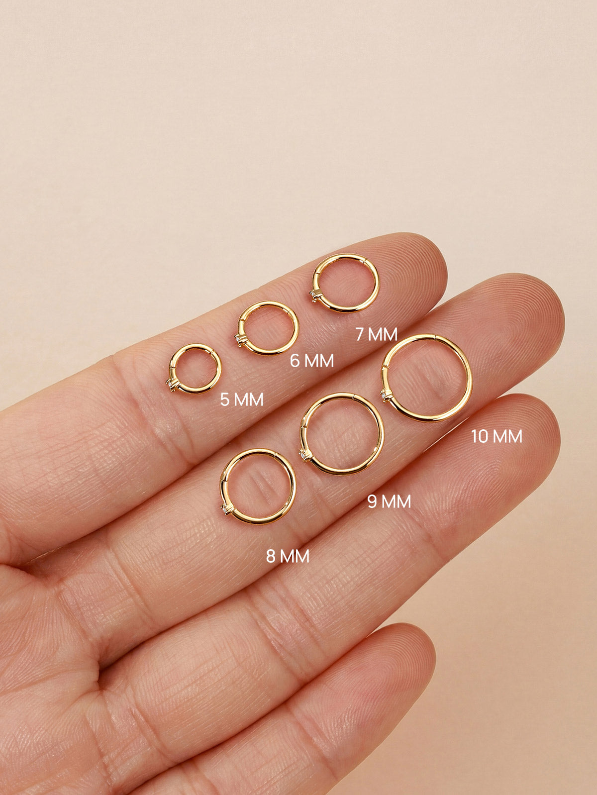 KOSINER diamond clicker hoops ranging 5mm through 10mm laid across fingertip with printed size markings to visualize diameter differences