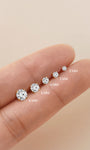 KOSINER lab-grown diamond flat back studs sized 2mm, 3mm, 4mm, 5mm, 6mm laid across fingertip to display scale difference of round brilliant gemstones in four-prong solid gold settings