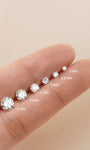 KOSINER moissanite flat back studs in 2mm to 6mm sizes laid on fingertip, showing visual scale difference of round brilliant-cut gemstones with four-prong gold settings