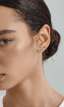 Elegant everyday styling with KOSINER Seaspritz tiny mermaid tail flat back stud on earlobe, model with neat low bun and plain neutral top, soft background showcasing petite wearable marine piercing jewelry