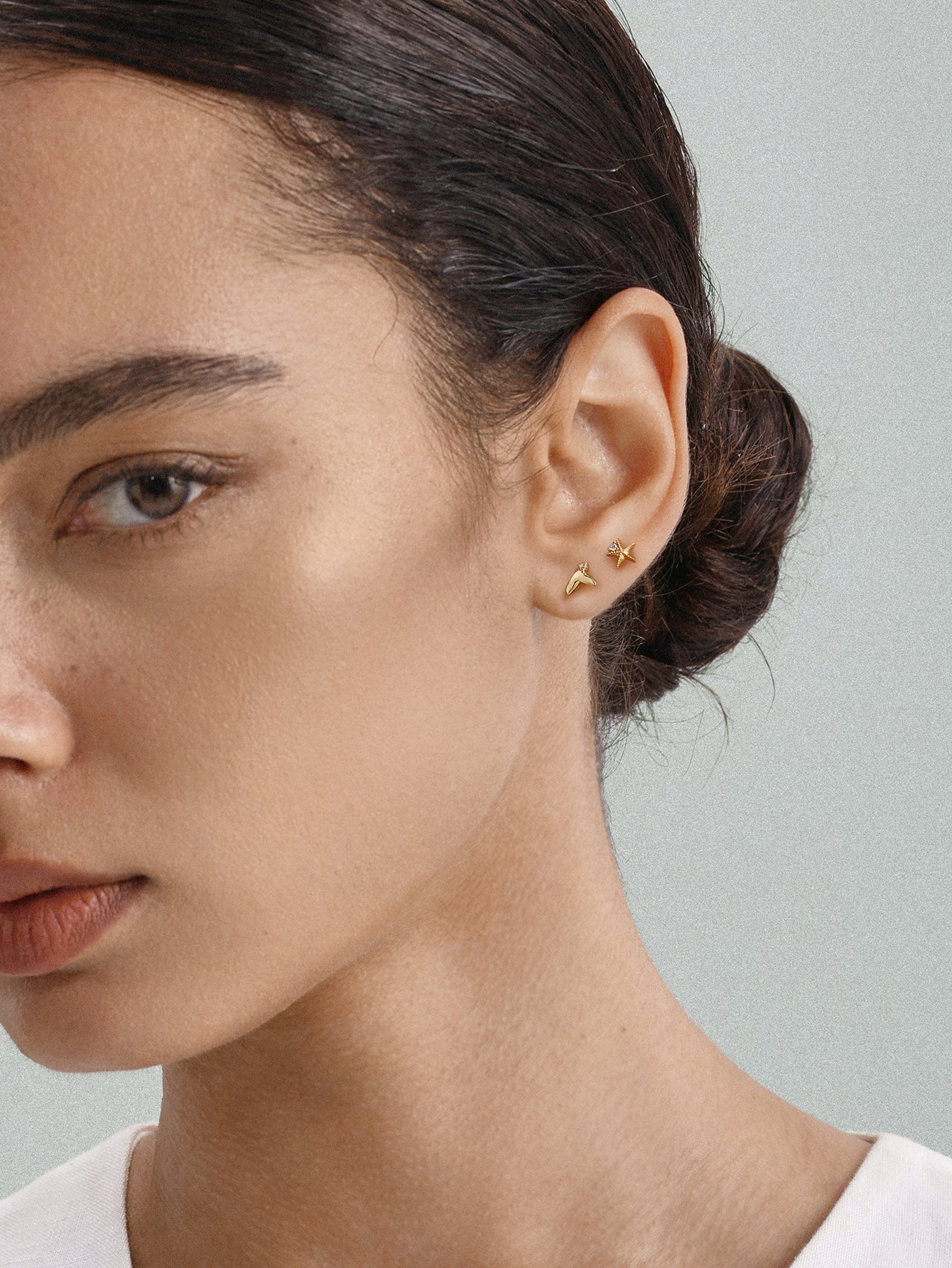 Elegant everyday styling with KOSINER Seaspritz tiny mermaid tail flat back stud on earlobe, model with neat low bun and plain neutral top, soft background showcasing petite wearable marine piercing jewelry