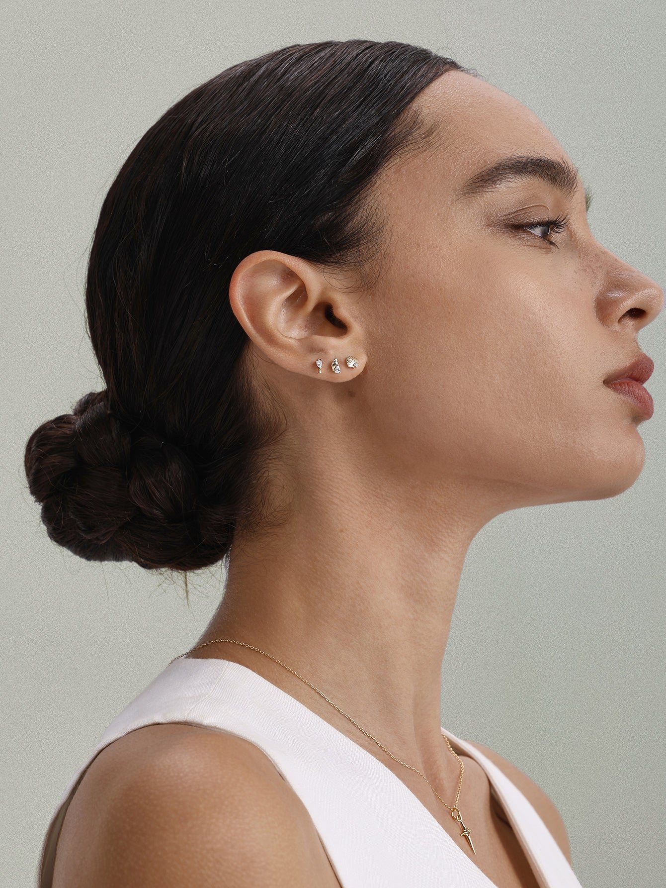 Extreme close-up shot of earlobe styled with KOSINER 14K gold seashell flat back stud paired with wine glass and other mini ocean piercing studs, delicate minimalist daily three-piece ear stacking design