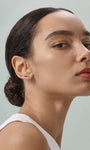 Elegant everyday styling with KOSINER Seaspritz tiny ice cream flat back stud on earlobe, model with neat low bun and plain neutral top, soft neutral background showcasing petite wearable seasonal piercing jewelry
