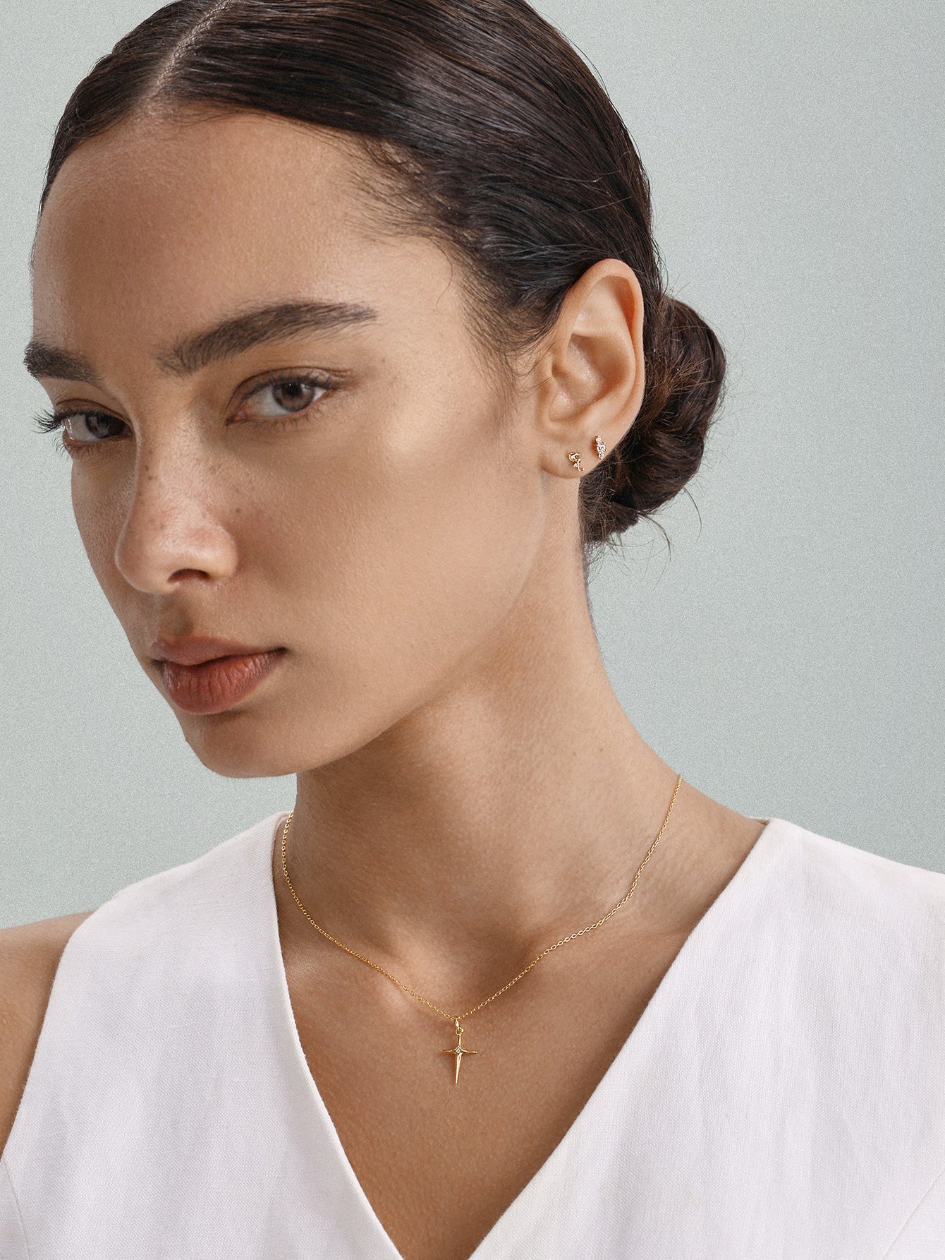 Elegant everyday styling with KOSINER Seaspritz tiny seahorse flat back stud on earlobe, model with neat low bun and plain neutral top, soft background showcasing petite wearable marine piercing jewelry