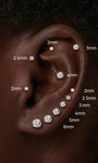Close-up of curated ear styling showcasing KOSINER 14K solid gold round moissanite flat back studs in sizes 2mm, 2.5mm, 3mm, 4mm, 5mm, 6mm, arranged across helix, tragus and earlobe piercings for size reference