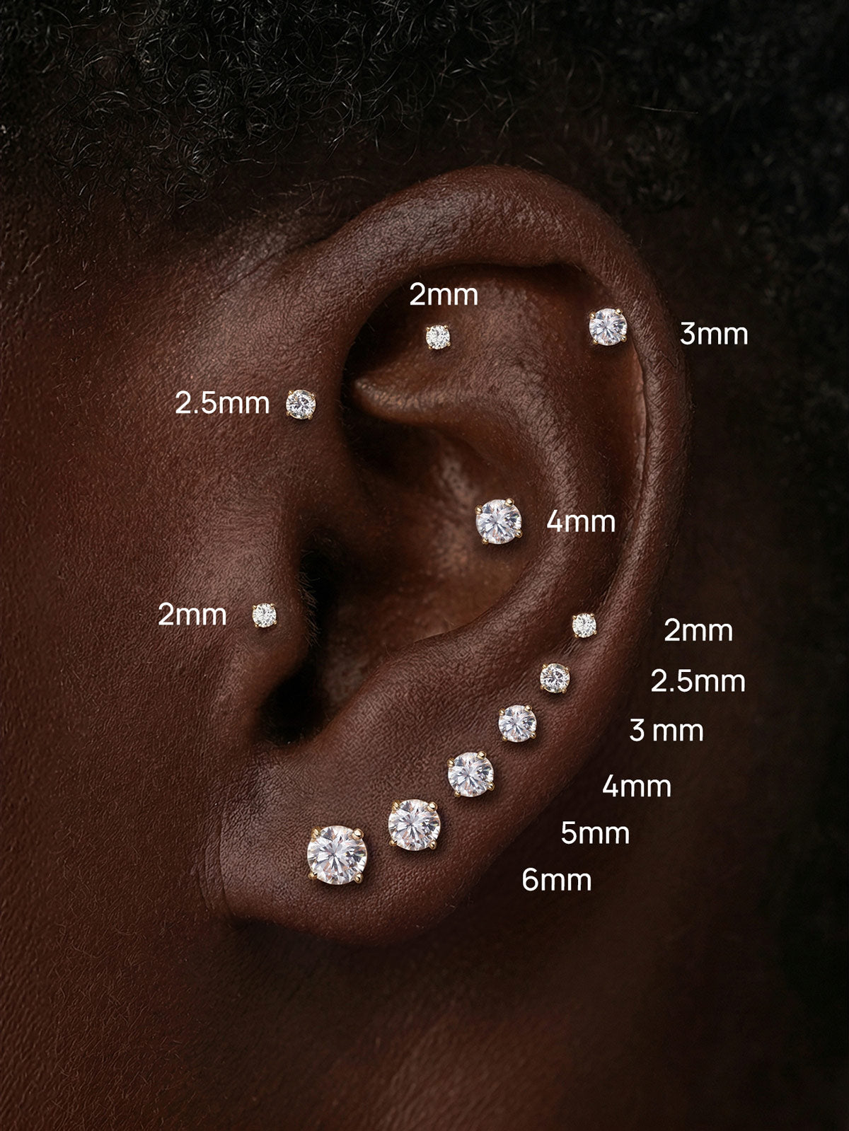 Close-up of curated ear styling showcasing KOSINER 14K solid gold round moissanite flat back studs in sizes 2mm, 2.5mm, 3mm, 4mm, 5mm, 6mm, arranged across helix, tragus and earlobe piercings for size reference