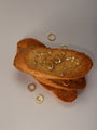 Aesthetic food-themed jewelry flat lay featuring KOSINER smooth oval drop gold hoops mixed with star chain dangling piercings and pavé crystal clicker hoops, arranged on stacked toast slices against neutral light gray background