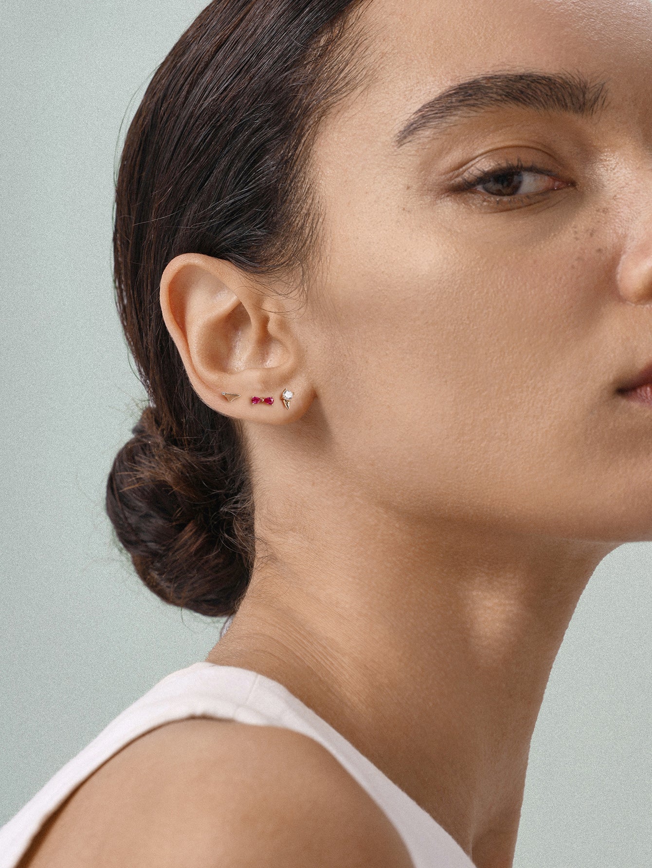 Daily minimalist styling with KOSINER Seaspritz bikini flat back studs on earlobe, model with sleek low bun and plain tank top, soft neutral background showing the delicate wearable design of vacation piercing jewelry