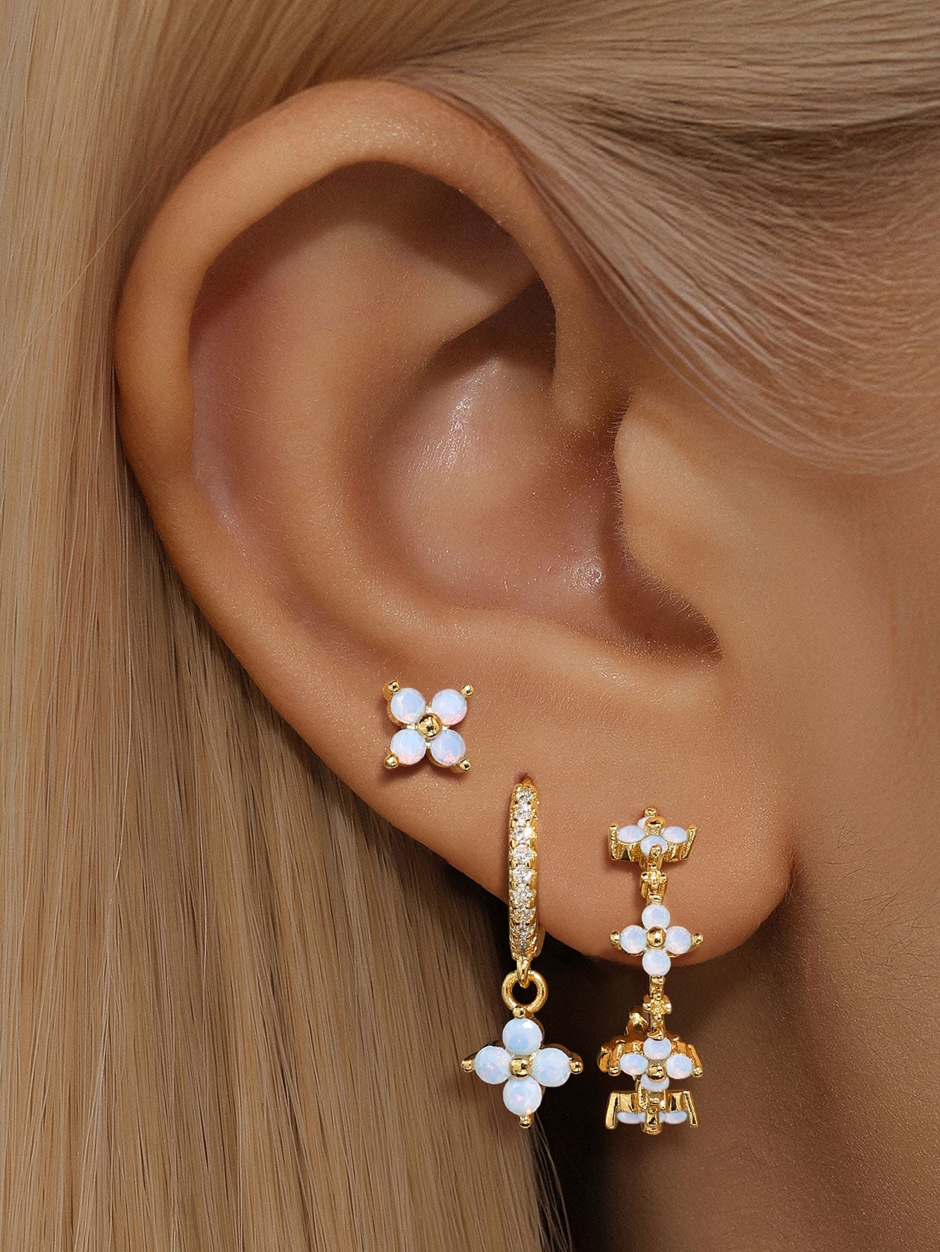 Collection of gold plated sterling silver earrings featuring light blue floral zirconia and crystal accents on a woman's ear.