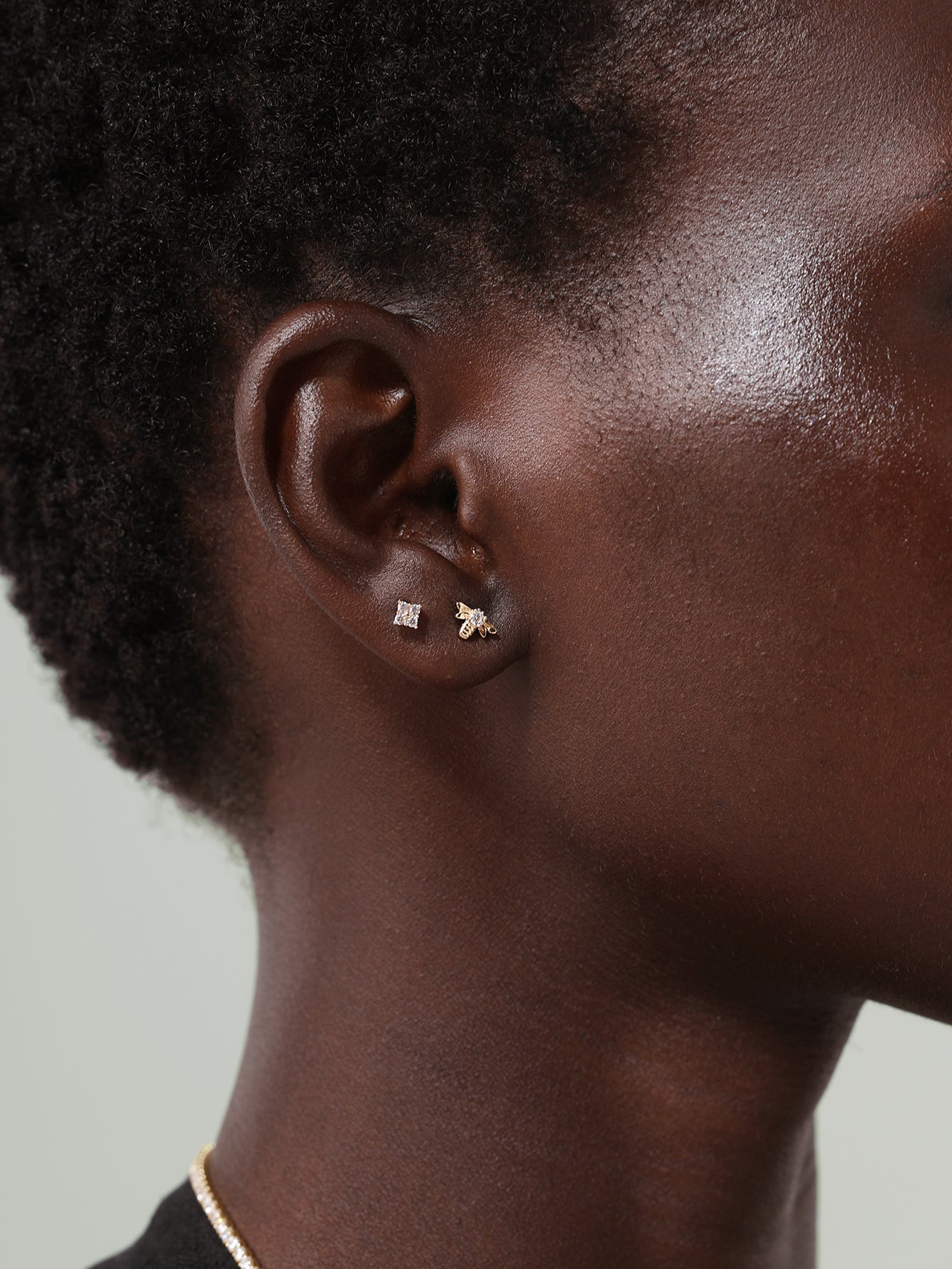 Model wearing 14K solid gold bee stud and square stud earrings with clear cubic zirconia on ear.