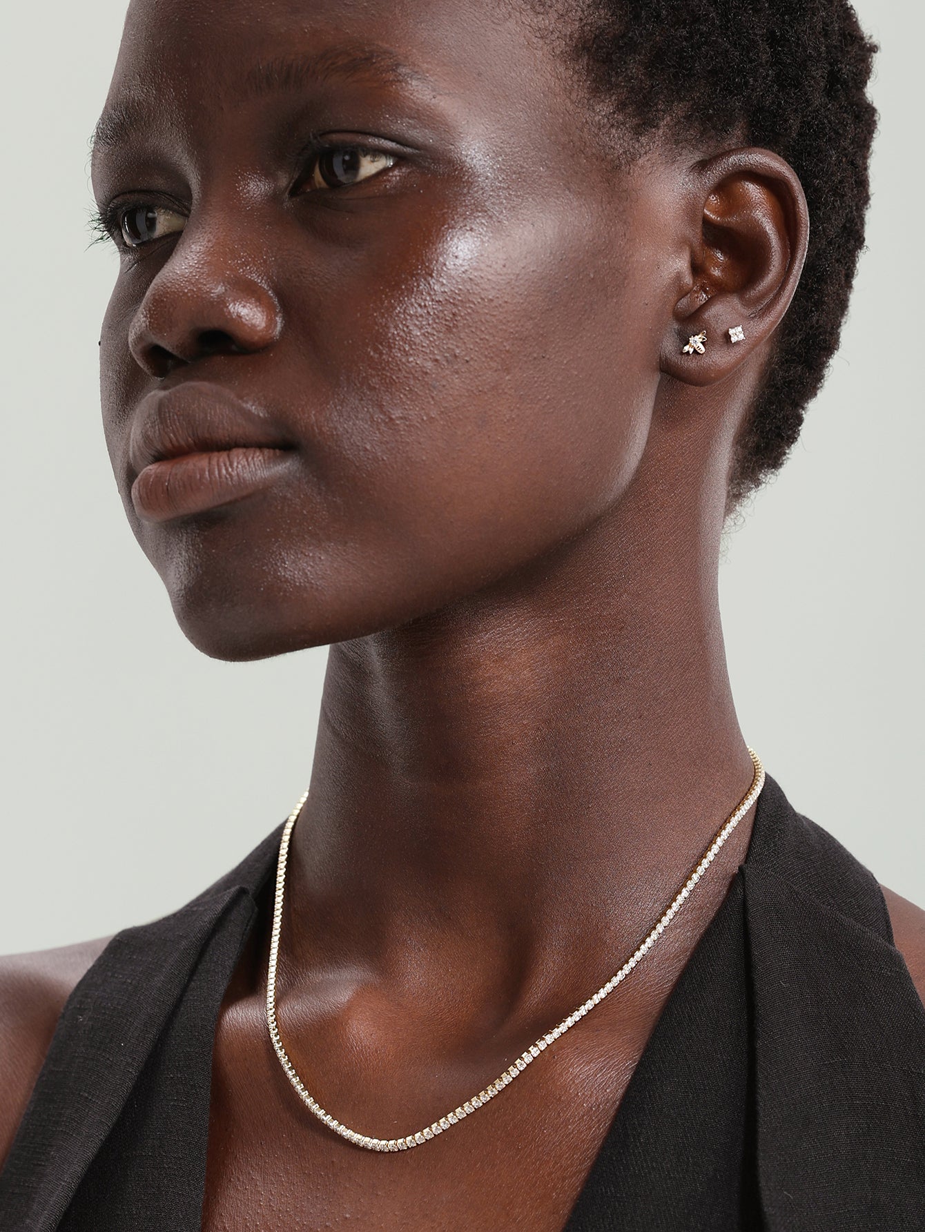 Model wearing 14K solid gold square stud and bee stud earrings with clear cubic zirconia stones.