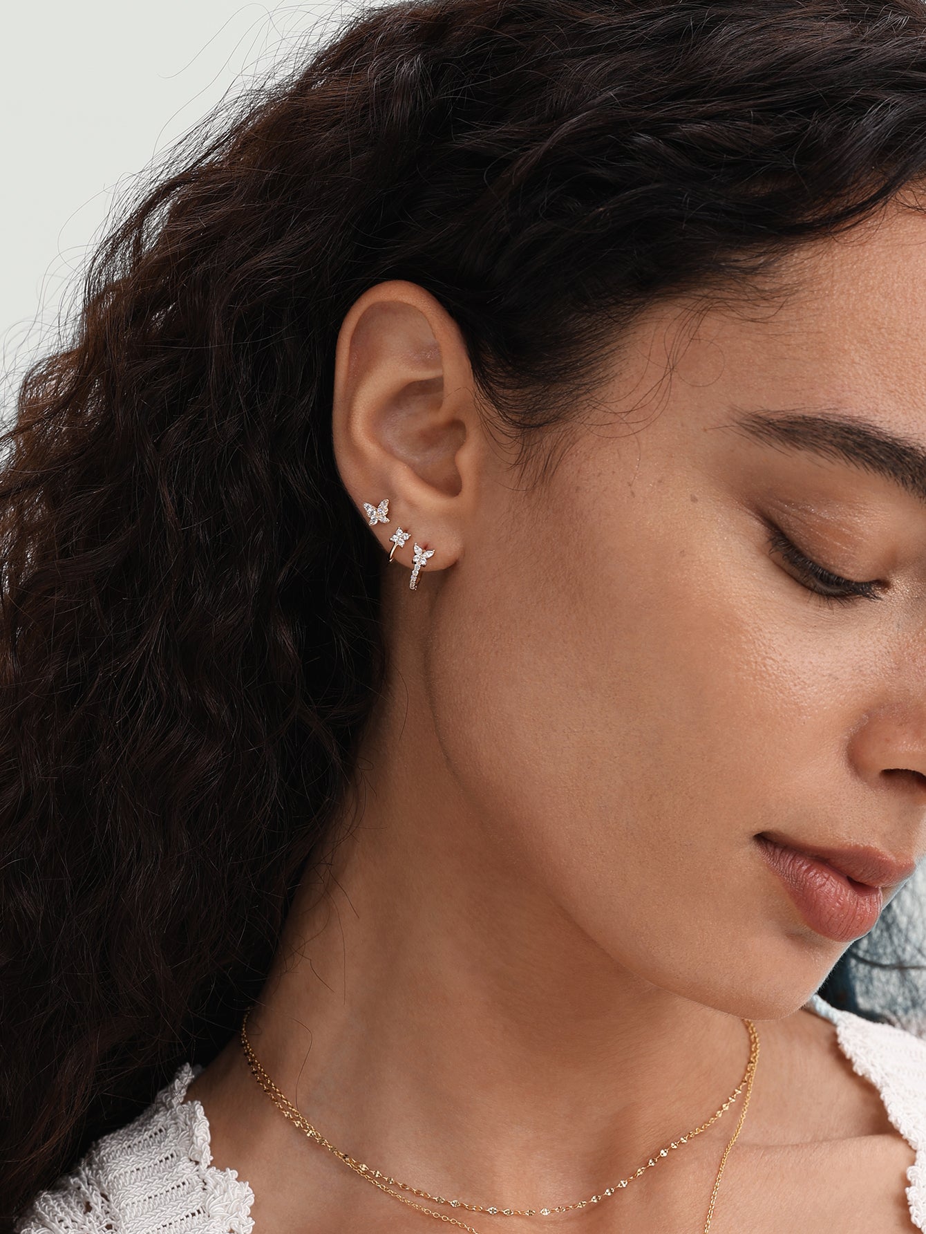 14K gold huggie hoop earrings with butterfly and flower designs, adorned with cubic zirconia, shown on a model's ear.