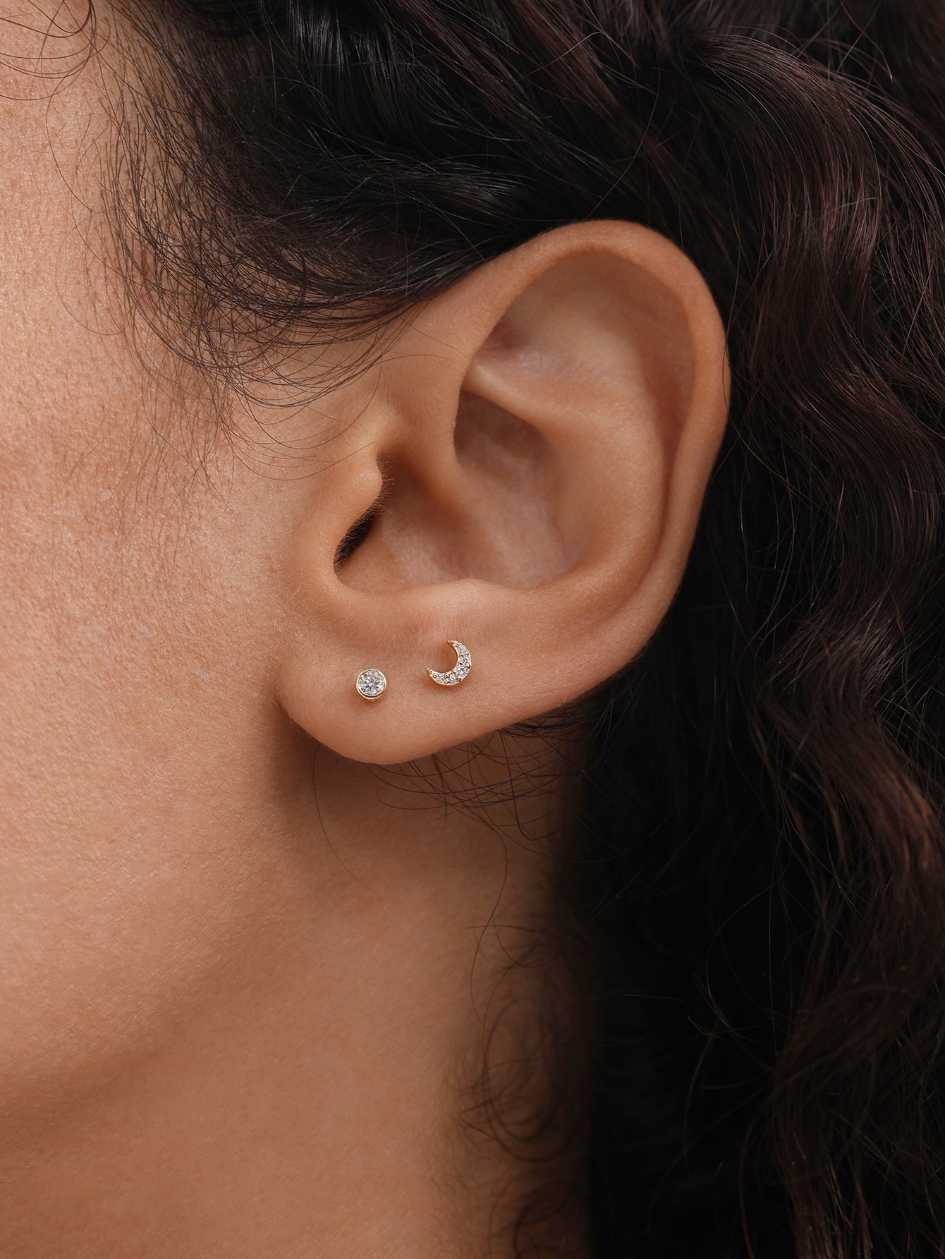 14K solid gold moon stud piercing with clear stones and flat back on ear, alongside a small round stud.