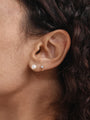 14K solid gold mini huggie hoop earring with a sparkling cubic zirconia, shown on earlobe next to a pearl stud.
