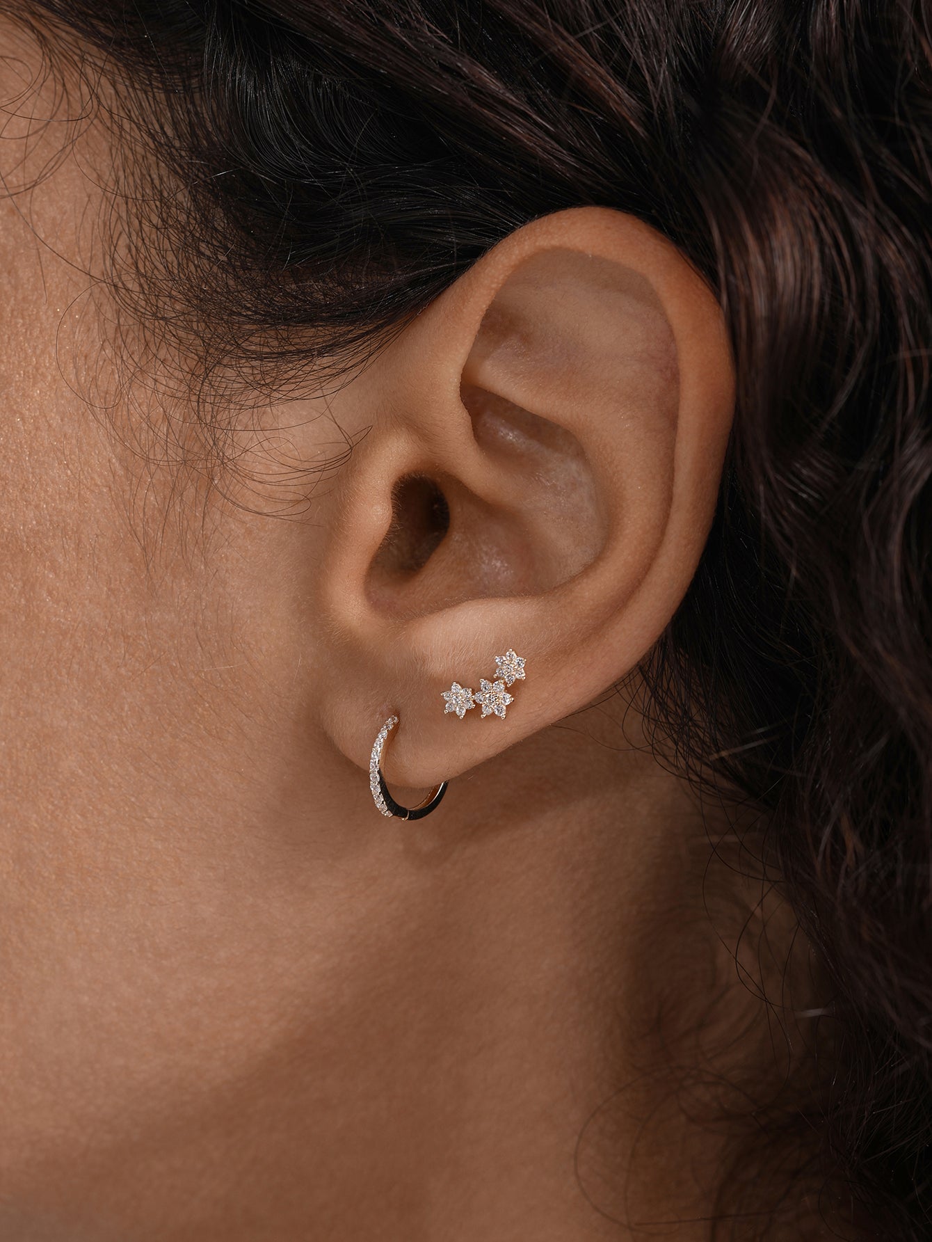 Model wearing 14K solid gold huggie earring with cubic zirconia, paired with star stud earrings.