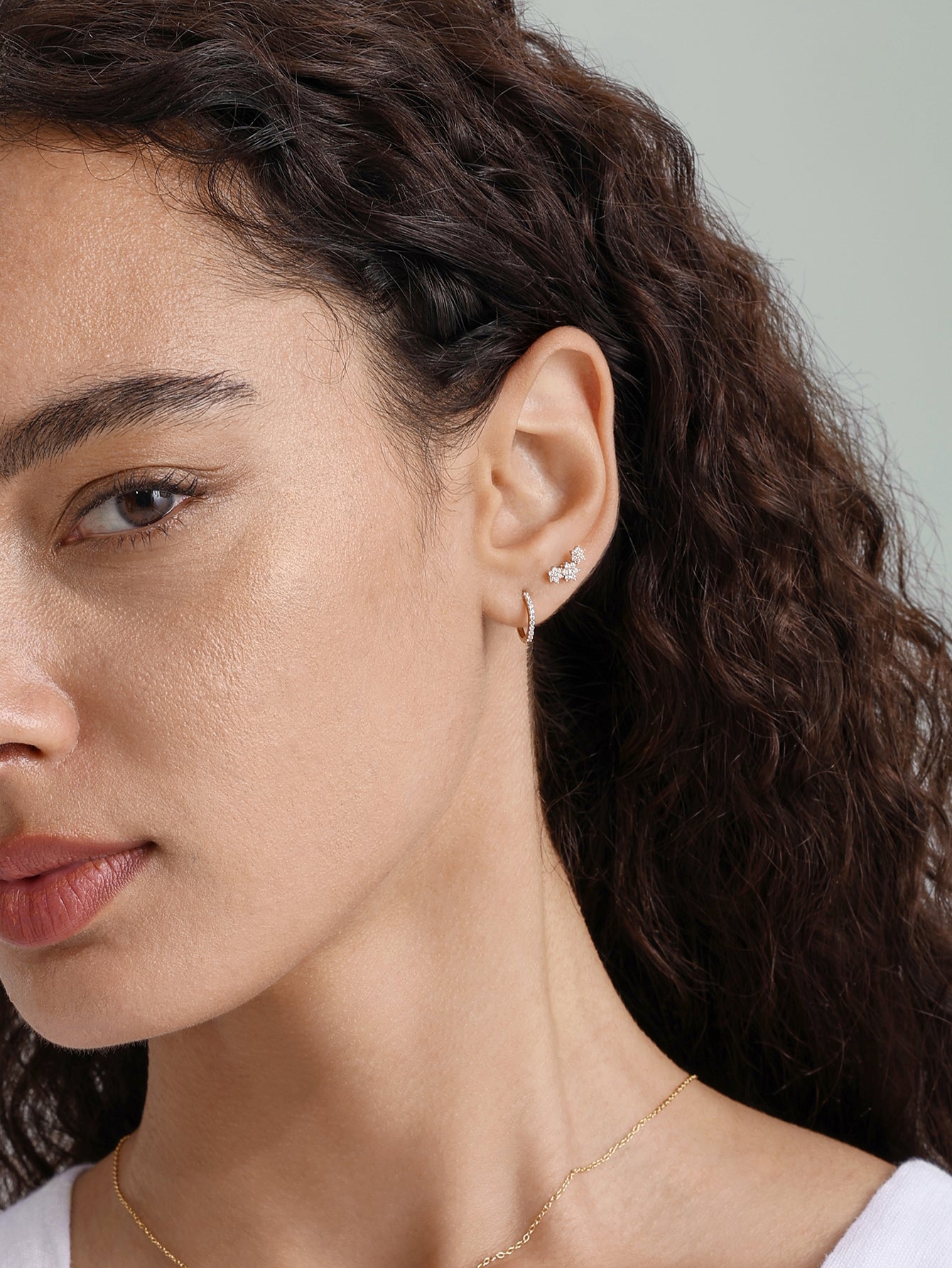 Model wearing 14K solid gold small hoop earrings with clear cubic zirconia crystals on earlobe and helix piercing.