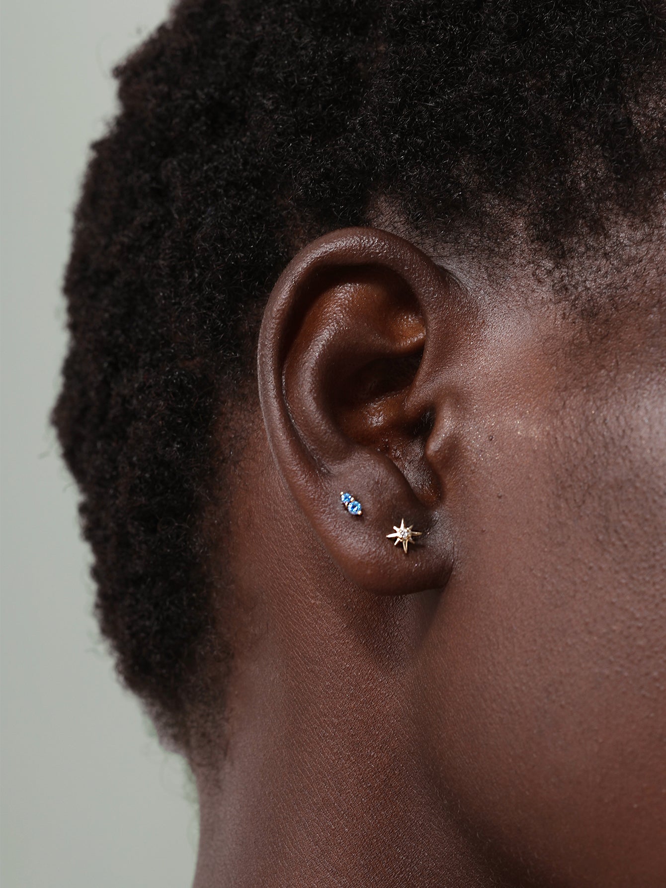 14K solid gold starburst stud with CZ center on ear, paired with blue stone stud.