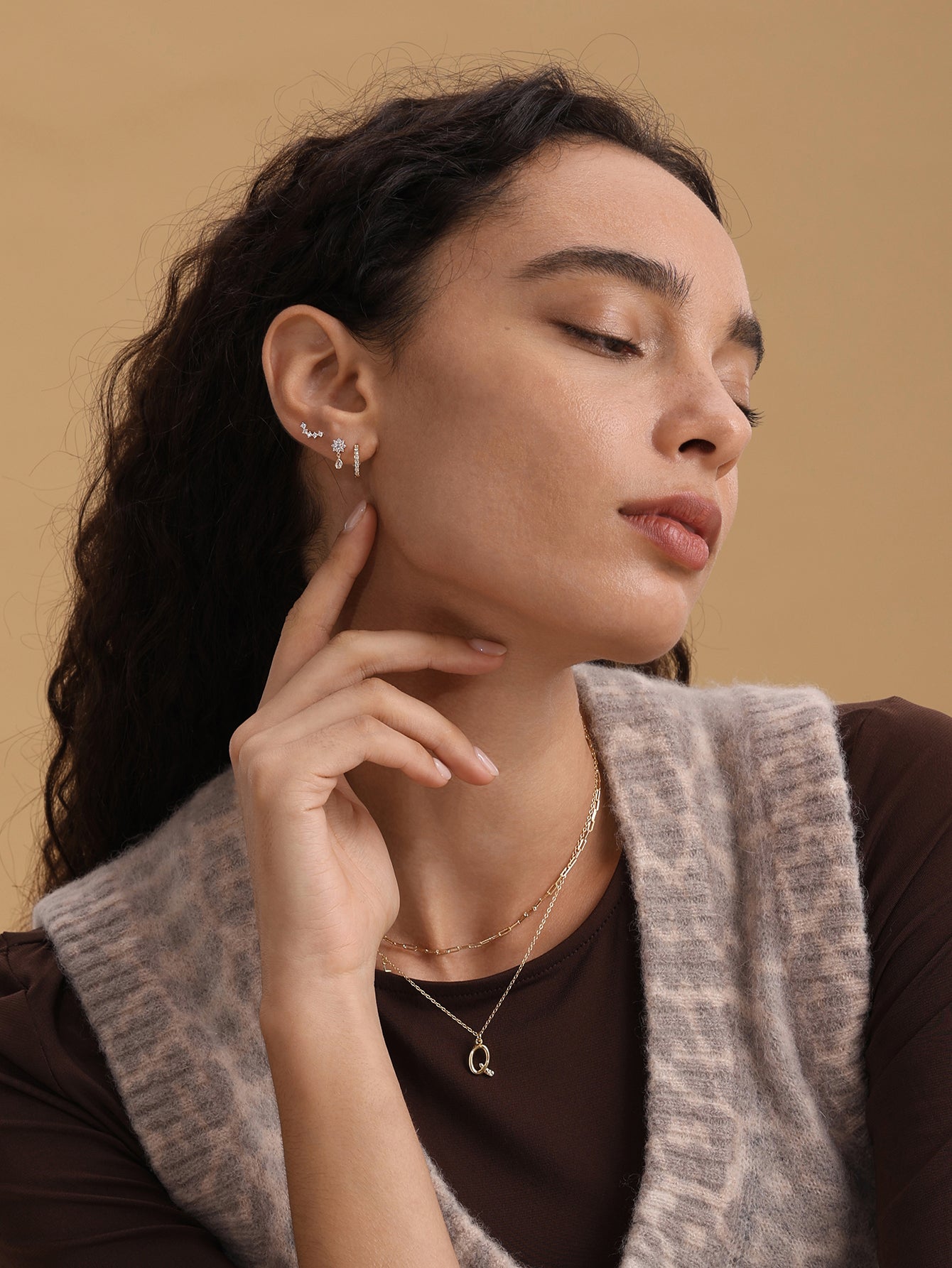 Model wearing 14K gold cubic zirconia hoop earring, bar stud, starburst stud, and initial Q necklace.