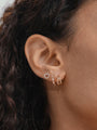Woman's ear featuring a 14K solid gold crystal hinged hoop clicker, alongside a heart stud and linear drop earring.