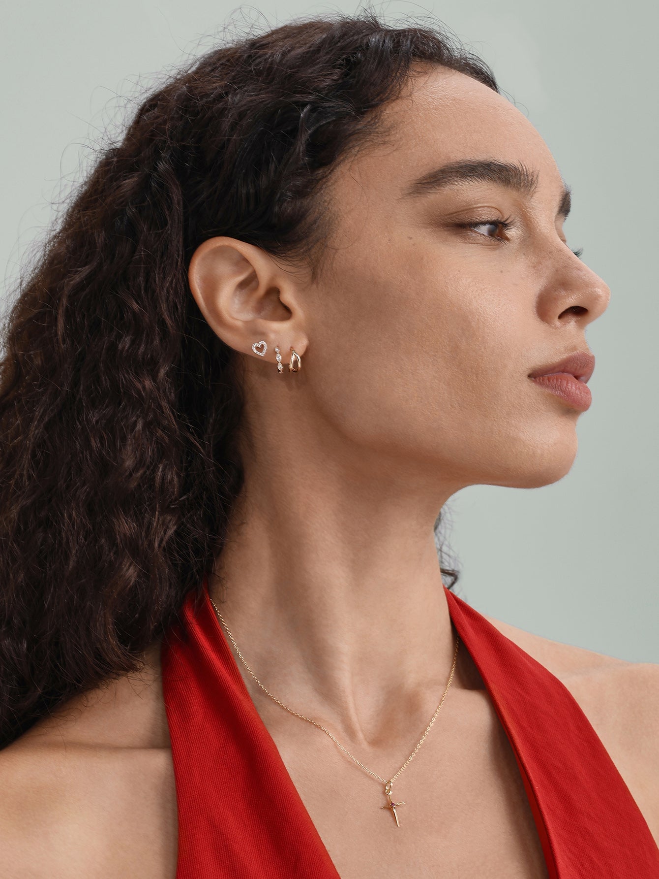 14K gold hinged hoop clicker with CZ crystals on a woman's ear, styled with a heart stud and cross necklace.