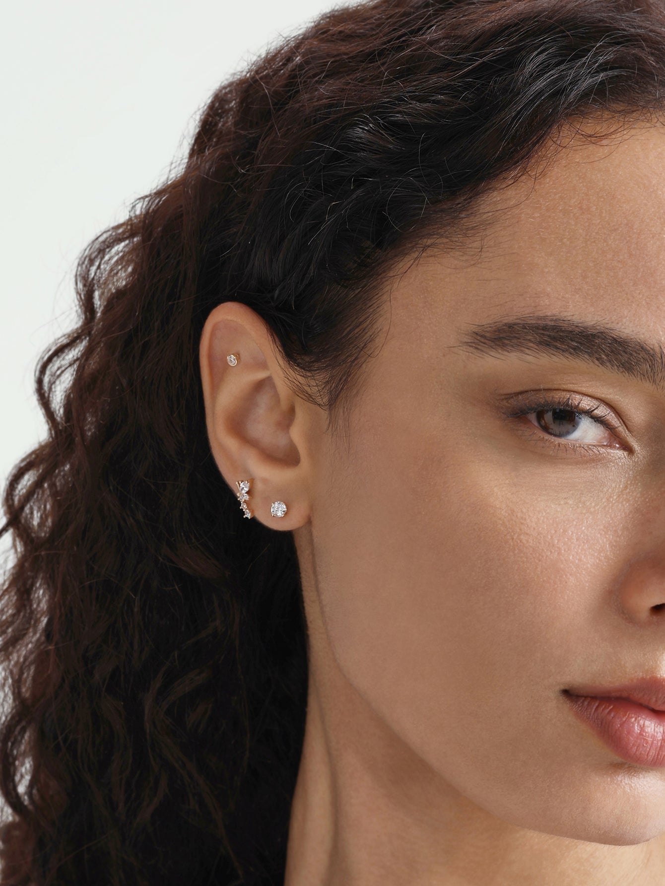 Model's ear with Kosiner 14K solid gold mini zircon ear piercing stud, sparkling, and another gold bar earring.