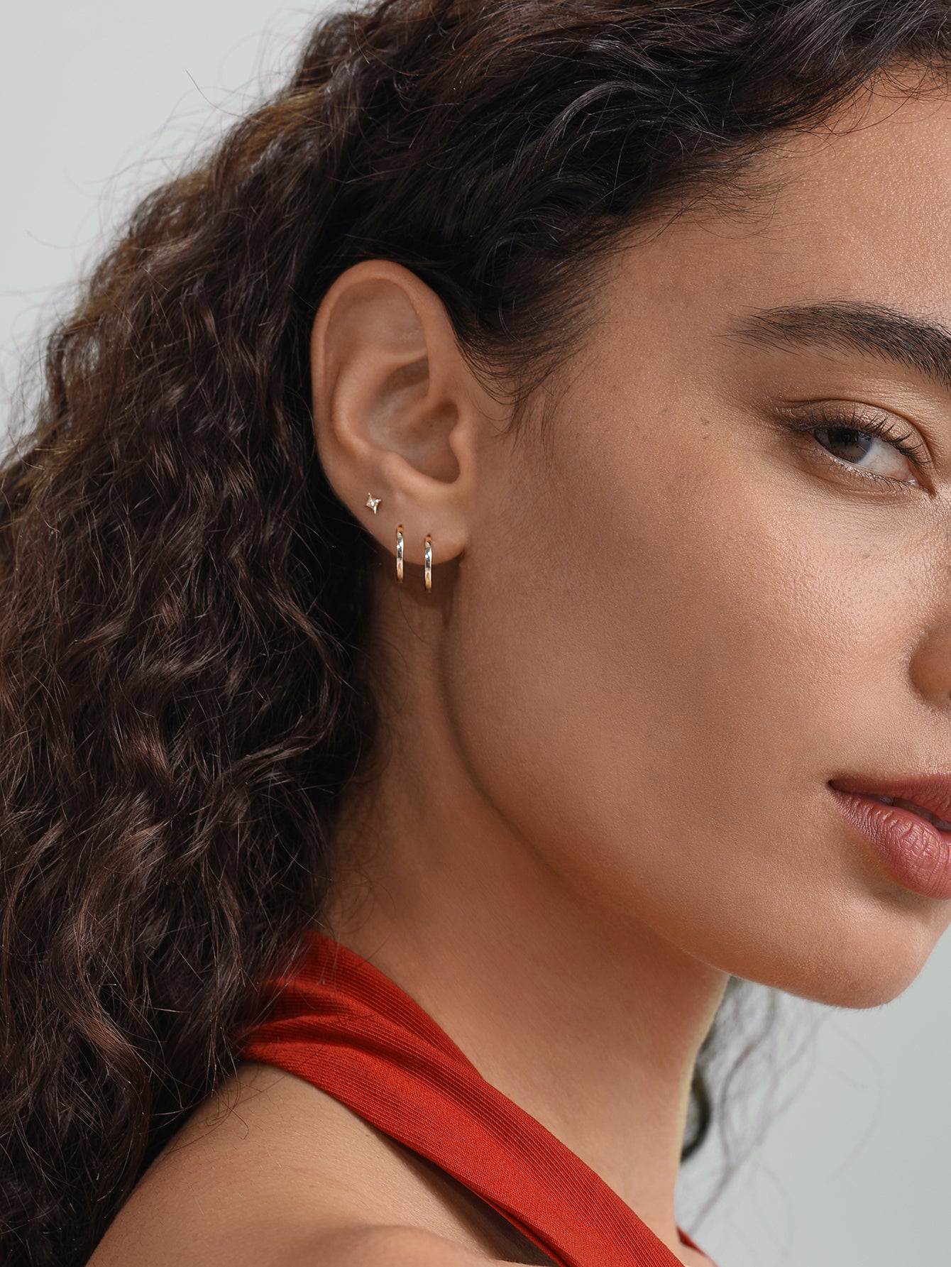 Woman's ear displaying a 14K solid gold simple hoop earring and a star stud earring with cubic zirconia.