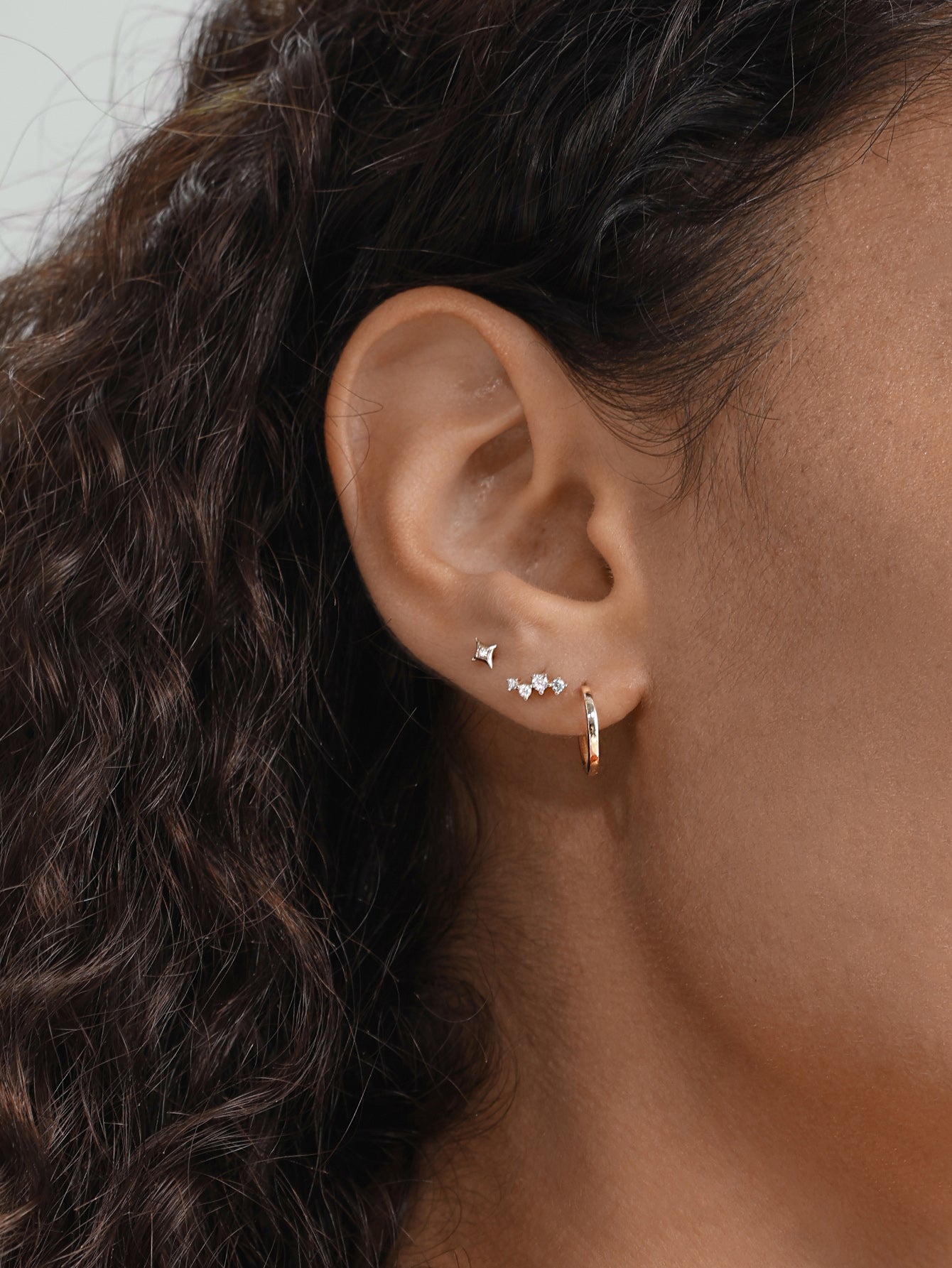 Model wearing a small, glossy 14K solid gold hoop earring with cubic zirconia studs on ear.