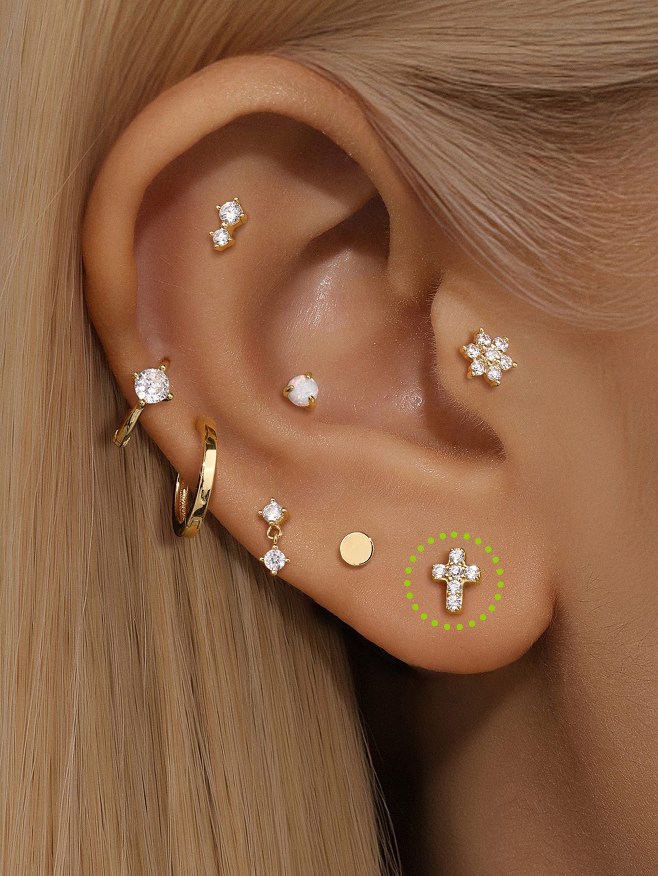 14K solid gold lucky cross ear piercing stud with cubic zirconia on human ear, shown with other gold earrings.