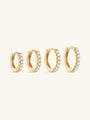 Four gold huggie hoop earrings with cubic zirconia stones in varying sizes. Showcasing product variations.