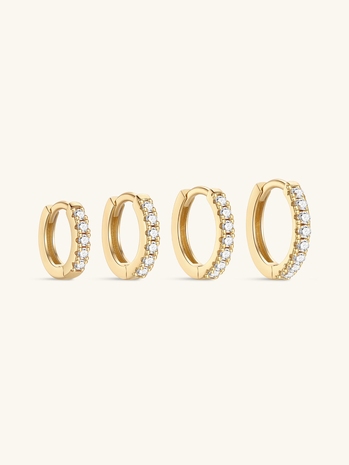 Four gold huggie hoop earrings with cubic zirconia stones in varying sizes. Showcasing product variations.
