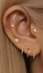 Piercing en forma de rayo de oro de 14 quilates con diamante de laboratorio, diseñado en la oreja de una mujer con otras joyas de oro.