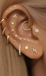Multiple 14K solid gold ear piercings with cubic zirconia and lightning bolt studs, styled on a human ear.