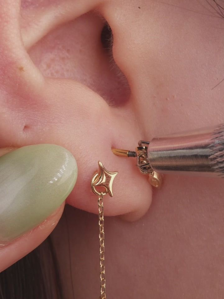 Brunette model curated ear stack styled with 14K gold dangling CZ flat back stud on earlobe, multi piercing lifestyle closeup