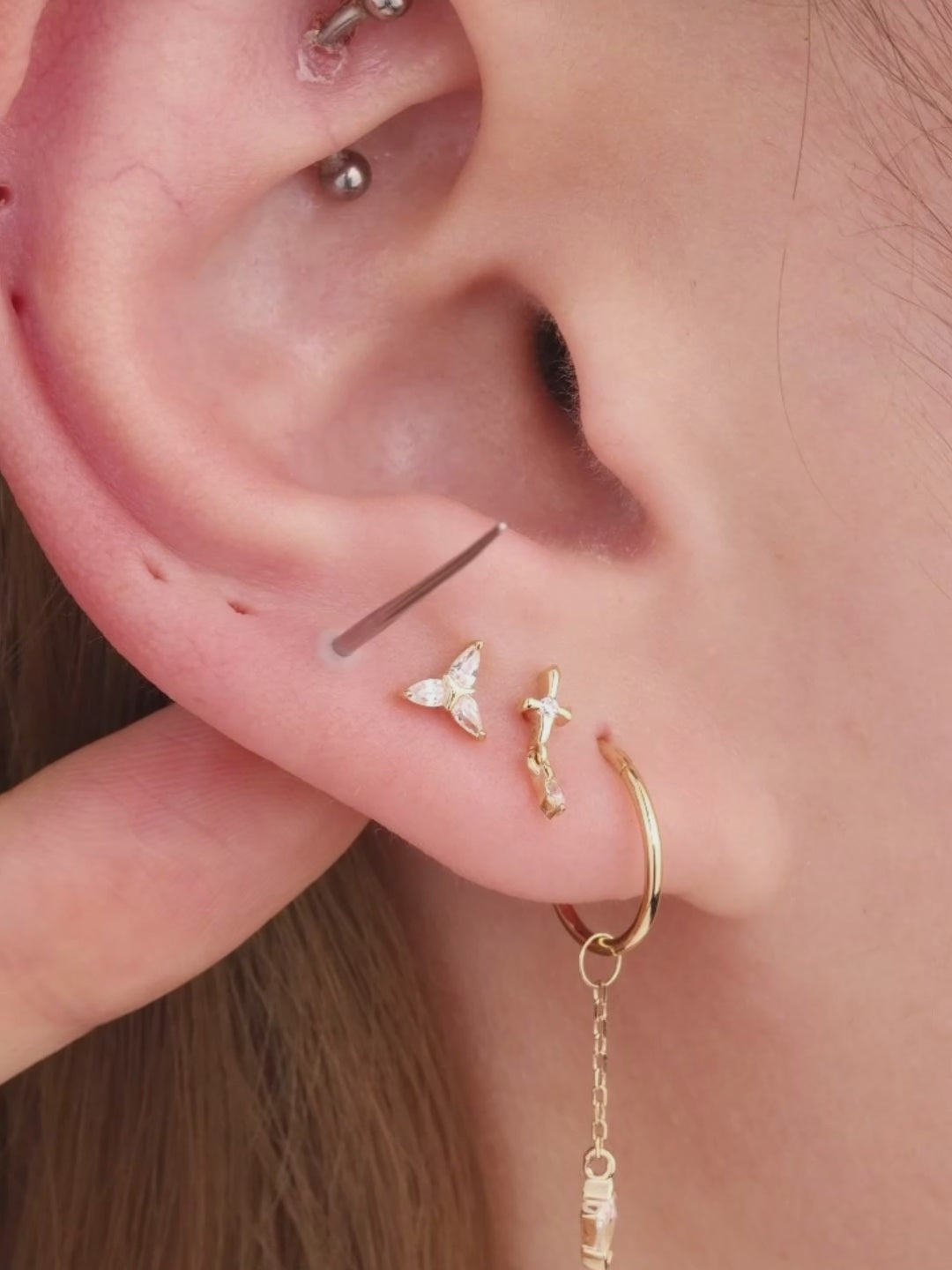 Blonde model ear stack styled with 14K solid gold Ankh cross cartilage stud on upper helix, layered curated multiple gold piercings lifestyle closeup