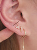 Blonde model ear stack styled with 14K solid gold Ankh cross cartilage stud on upper helix, layered curated multiple gold piercings lifestyle closeup