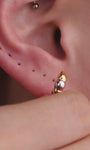 Sophisticated layered ear styling showcasing KOSINER Perléa beaded cross stud connected with delicate chain to teardrop outline piercing, paired with north star helix studs, marquise detail daith clicker, blue marquise eye stud and two-tone huggie hoop, trendy versatile curated ear layout