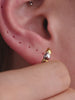 Sophisticated layered ear styling showcasing KOSINER Perléa beaded cross stud connected with delicate chain to teardrop outline piercing, paired with north star helix studs, marquise detail daith clicker, blue marquise eye stud and two-tone huggie hoop, trendy versatile curated ear layout